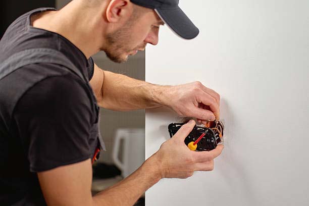 Person using a drill on a white wall doing electrical work
